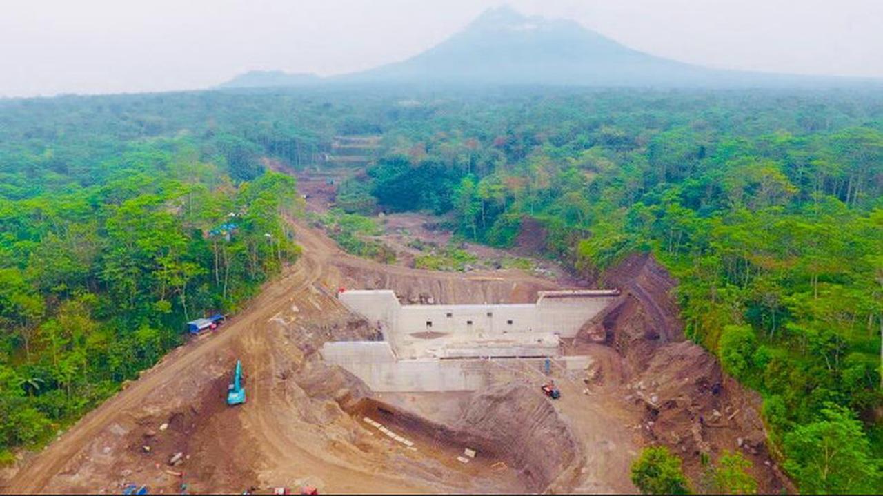 Pemandangan bangunan Sabo Dam beton di aliran sungai hulu lereng Gunung Merapi dengan latar belakang awan.