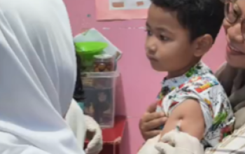 Petugas medis dari Puskesmas Bakti Jaya sedang memberikan imunisasi campak kepada seorang anak di sebuah Taman Kanak-kanak.
