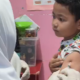 Petugas medis dari Puskesmas Bakti Jaya sedang memberikan imunisasi campak kepada seorang anak di sebuah Taman Kanak-kanak.