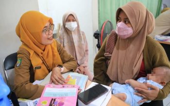 Seorang petugas kesehatan di Puskesmas sedang memberikan tetesan/suntikan imunisasi kepada anak balita yang didampingi ibunya.