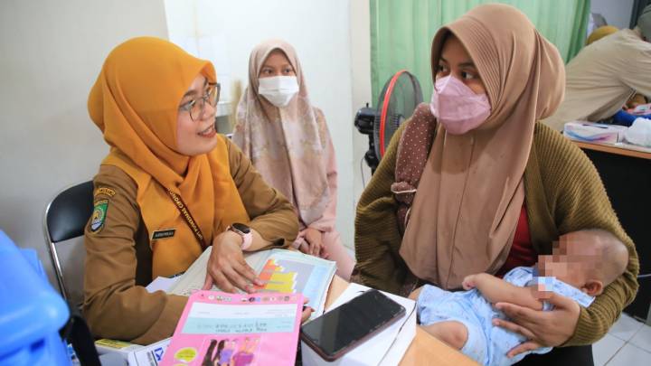 Seorang petugas kesehatan di Puskesmas sedang memberikan tetesan/suntikan imunisasi kepada anak balita yang didampingi ibunya.