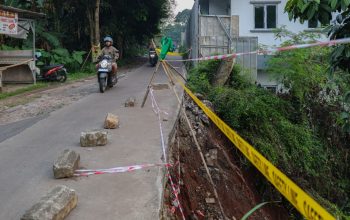 Petugas BPBD Tangsel sedang memasang garis pembatas (police line) dan rambu peringatan di sisi jalan yang longsor di Ciater.