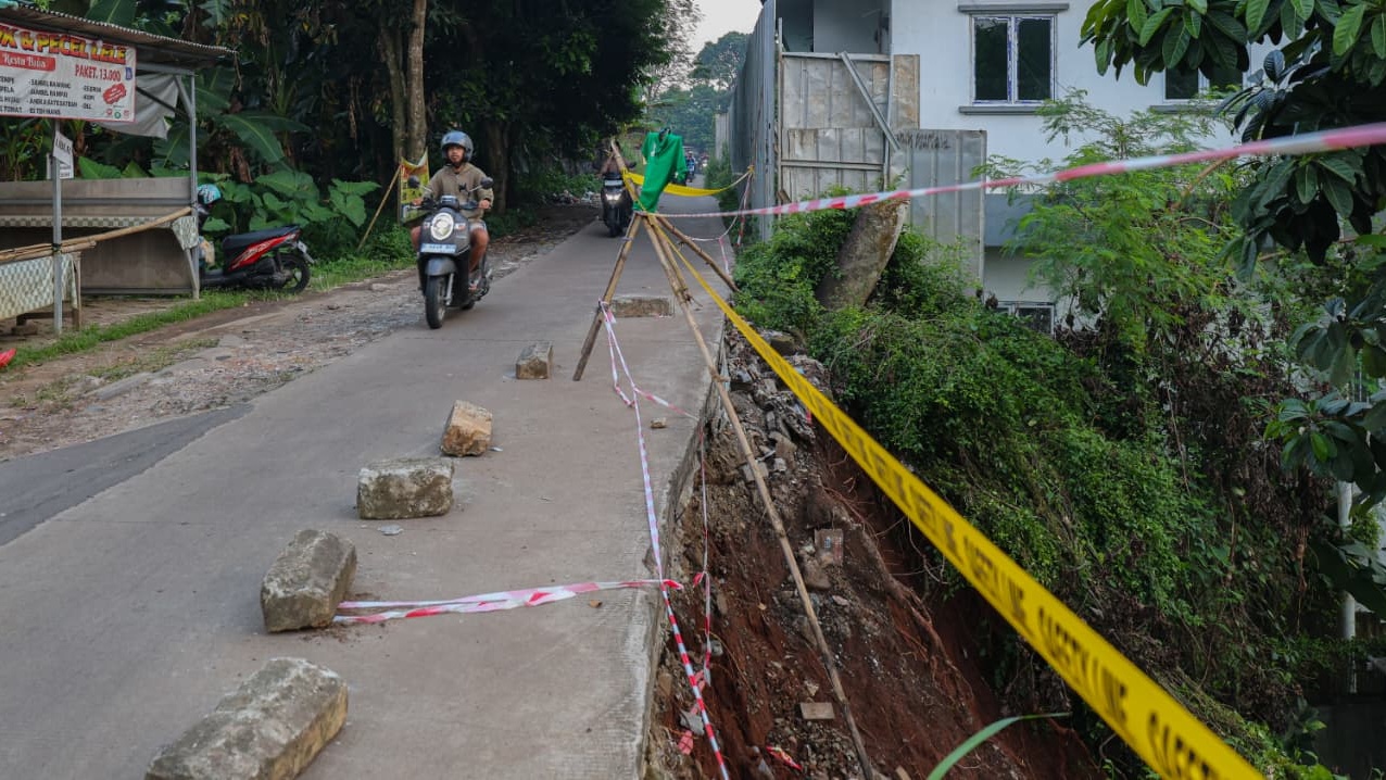 Petugas BPBD Tangsel sedang memasang garis pembatas (police line) dan rambu peringatan di sisi jalan yang longsor di Ciater.
